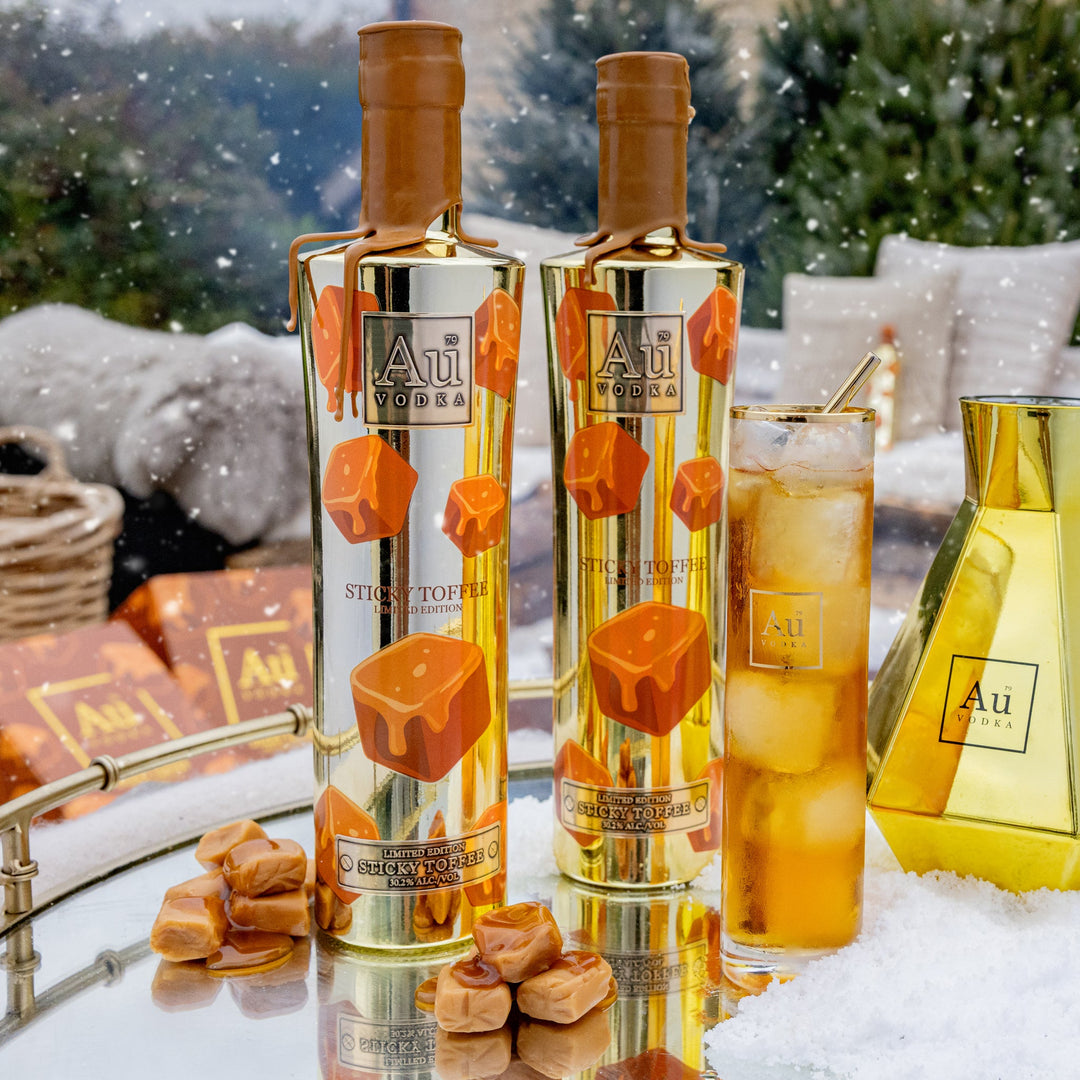 Two bottles of Au Vodka with Sticky Toffee candies and a cocktail in a snowy outdoor setting.
